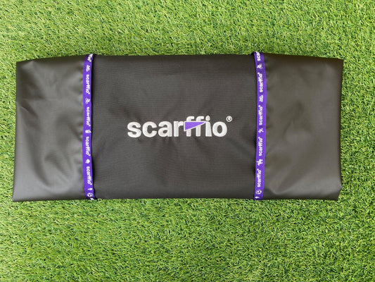 Showing a folded Custom Jet Black and Rich Purple scarffio® on a grass background. The folded scarffio® shows the contrasting Rich Purple embroidered cape and branded edging .