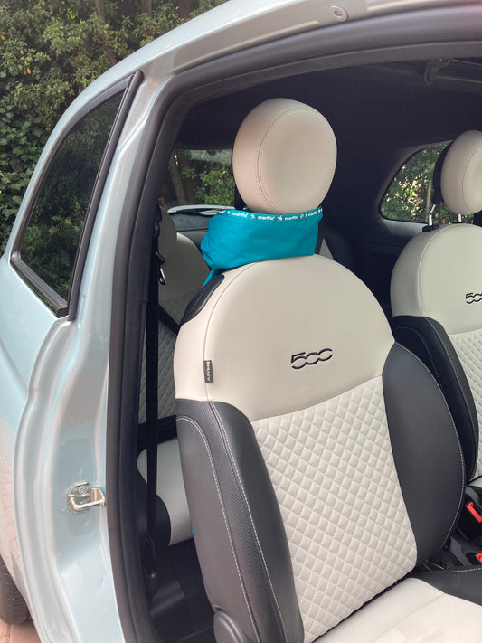 This image shows the interior of a Fiat 500 car, and a Wild Teal scarffio® stored in standby mode - tied around the headrest of the drivers seat, like a scarf. There is a small portion of the Wild Teal scarffio® showing between the headrest and the top of the seat, and the rest is draped over the back of the seat, out of shot, except for a tiny bit peeping out from behind the bottom of the seat. 