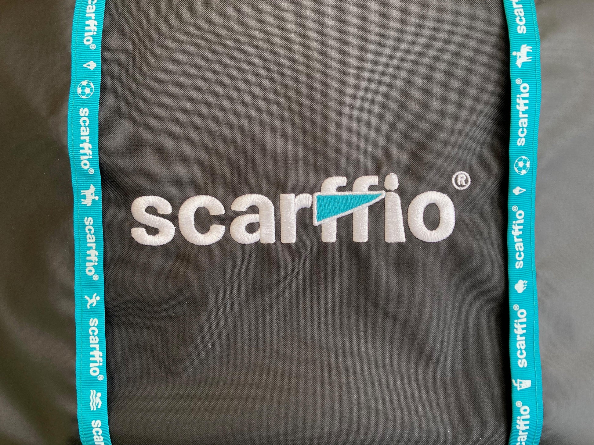This image shows a close up of the scarffio® embroidered logo with a Teal  cape , and matching teal edging on a Jet Black fabric.