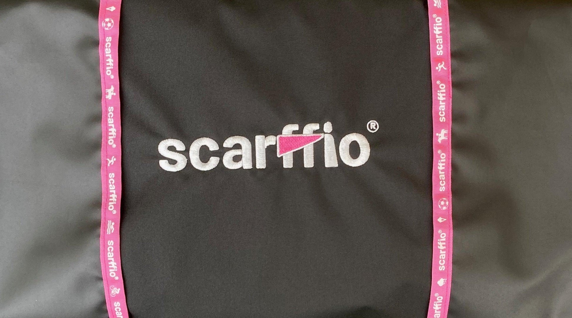This image shows a close up of the scarffio® embroidered logo with a Pink cape , and matching branded  Pink edging on a Jet Black fabric.