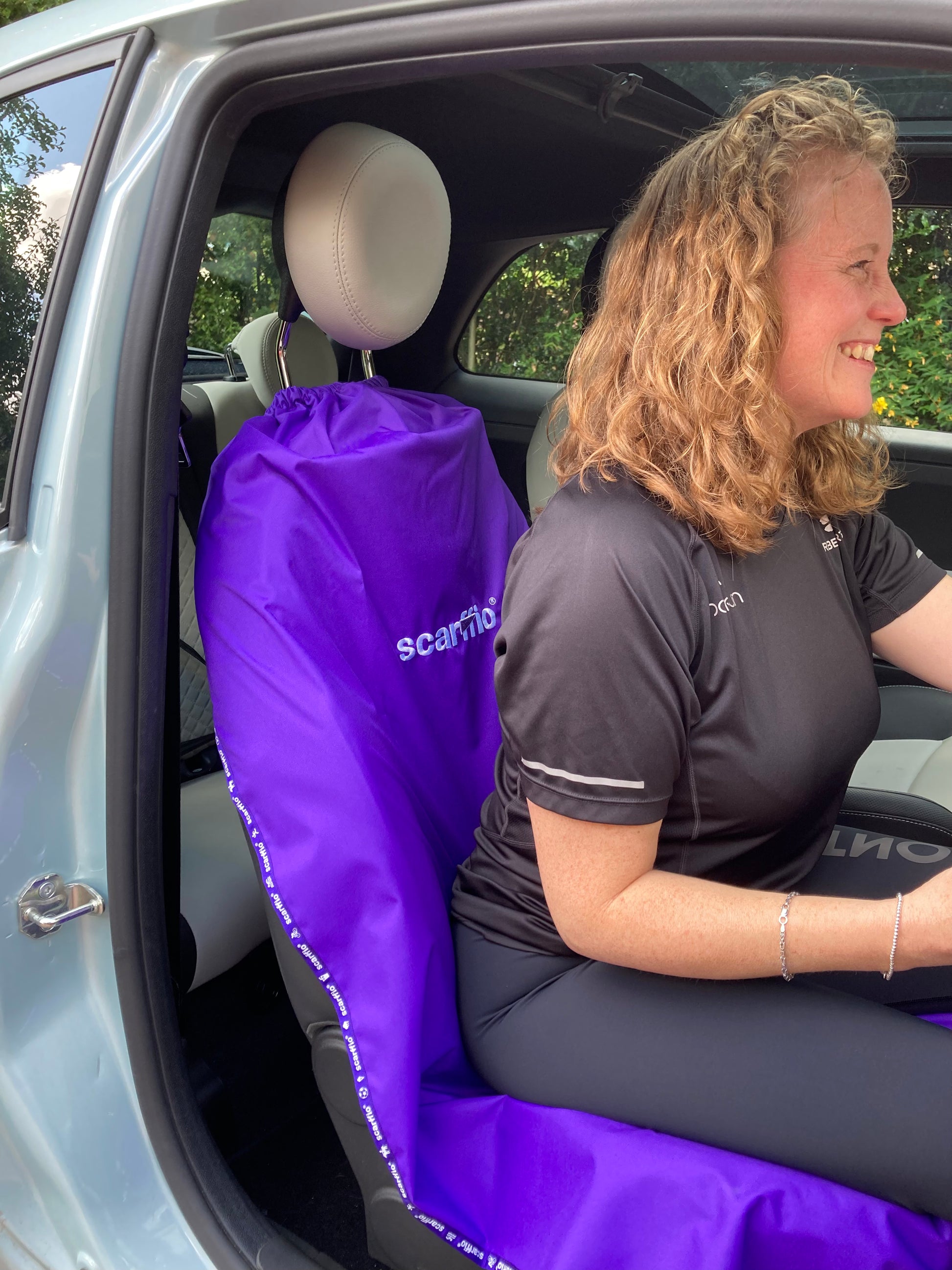 This image shows at the interior of a Fiat 500, with a Rich Purple scarffio® down on the drivers seat , with a smiling female driver in situ. 